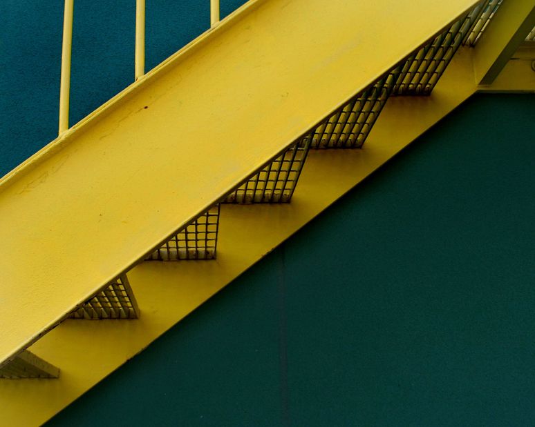 a detail image of a yellow grated stairway infront of a green building